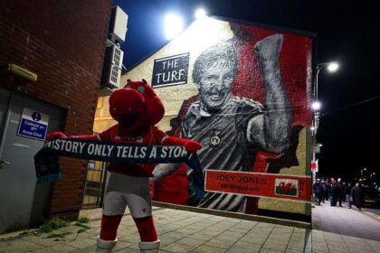 Wrexham mascot Wrex the Dragon stands in front of a Joey Jones mural