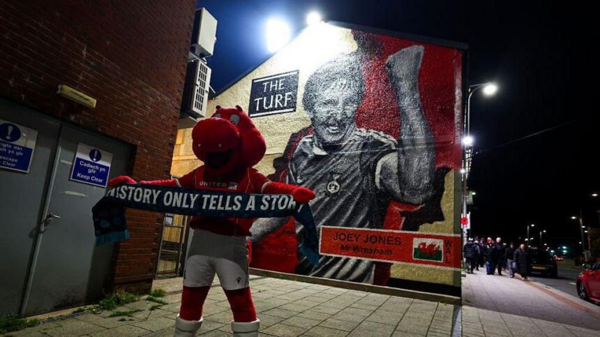 Wrexham mascot Wrex the Dragon stands in front of a Joey Jones mural