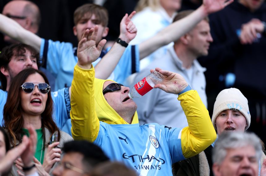 A Manchester City fan celebrates victory with a water bottle featuring the Arsenal logo after Sunday's game.