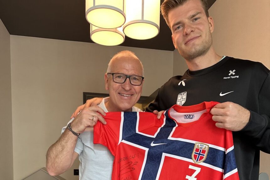 Gøran Sørloth and his son Alexander hold up a Norway shirt together. Alexander is playing for Norway in the World Cup. Gøran played for the national team in 1994.